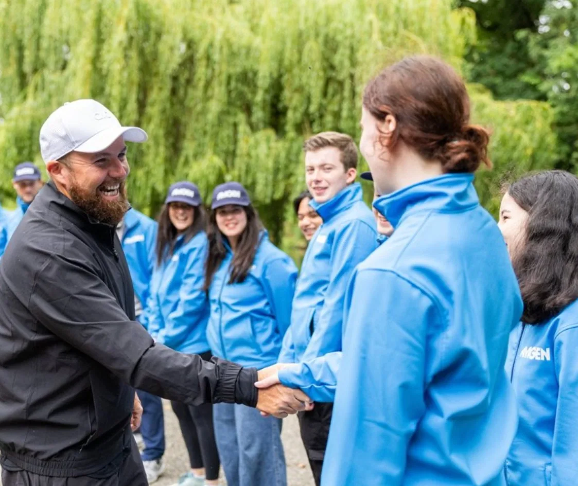 Shane Lowry shaking hands with Amgen colleagues in blue team jackets